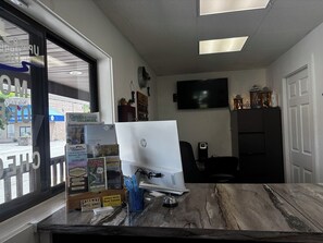 A hotel reception desk with a desktop computer, a window with a view of the outside, and various informational brochures. - Upper Delaware Inn (Hancock)