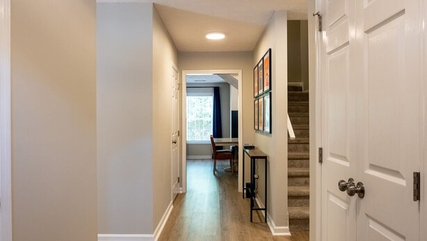 Un couloir avec un plancher en bois, un escalier et une porte sur le côté droit.