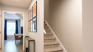 Un couloir avec un escalier, un coin repas avec une table et des chaises, et des tableaux encadrés accrochés au mur.