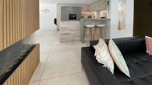 A modern living room with a black sofa, a wooden accent wall, and a kitchen in the background. - Pet friendly home in Ballum with sauna (Ballum)