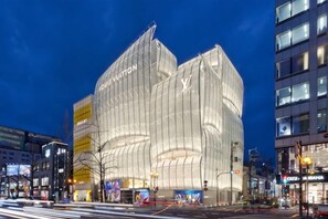 Ein modernes Gebäude mit einer markanten, gebogenen Glasfassade und dem gut sichtbaren 'Louis Vuitton'-Logo.