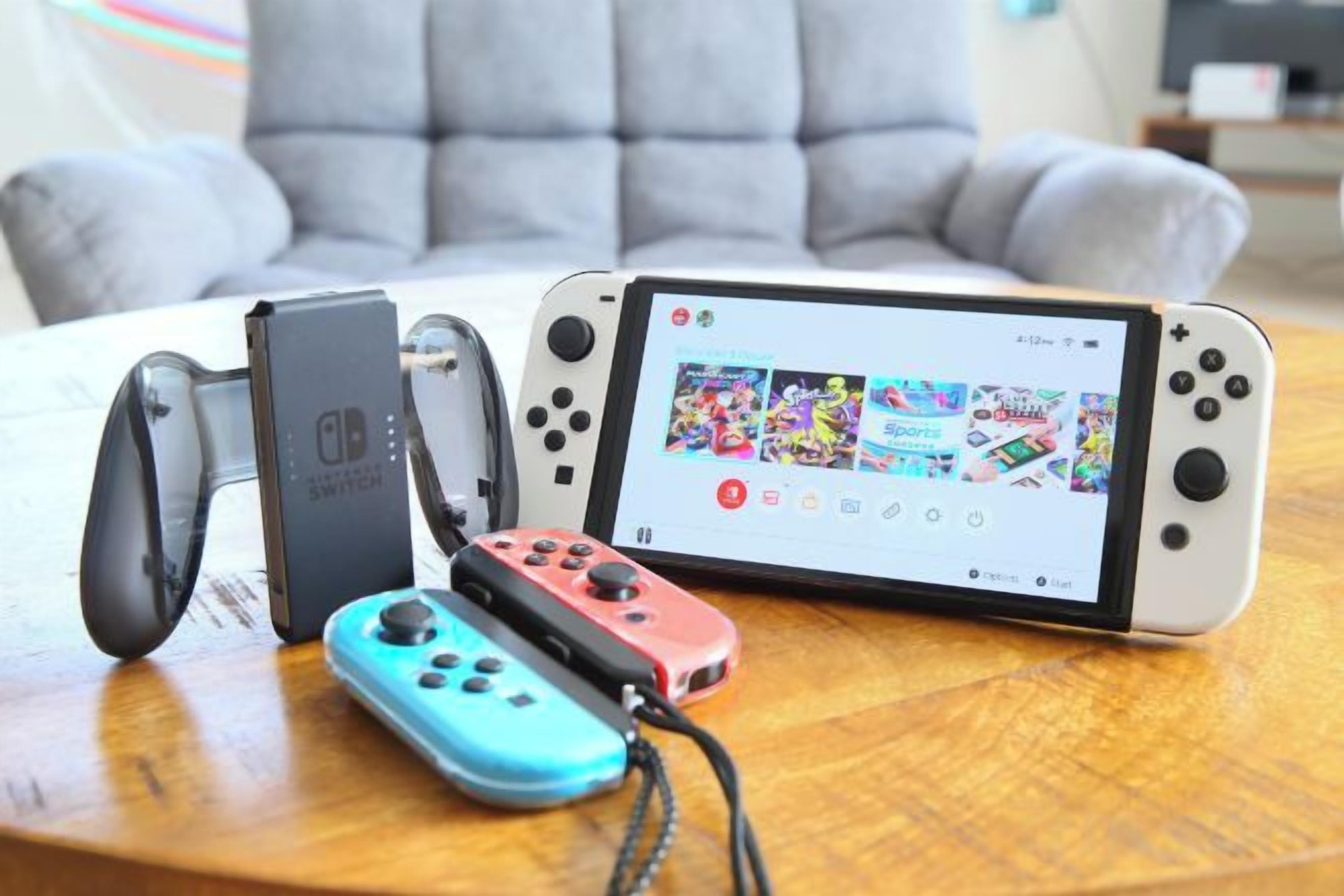 Una consola Nintendo Switch con una biblioteca de juegos en la pantalla, un dock de carga y dos mandos Joy-Con sobre una superficie de madera.