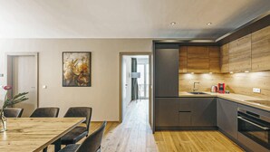 Une cuisine moderne avec des meubles en bois, un four encastré et un coin repas comprenant une table et des chaises en bois.