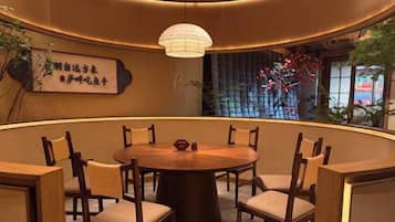 Una mesa redonda con sillas en una habitación con pared curva, una lámpara colgante y un muro decorativo con plantas.