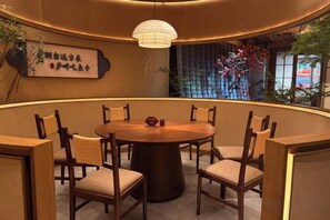 A round table with chairs in a room with a curved wall, a hanging light fixture, and a decorative wall with plants. - Yilin International Hotel (Hefei)