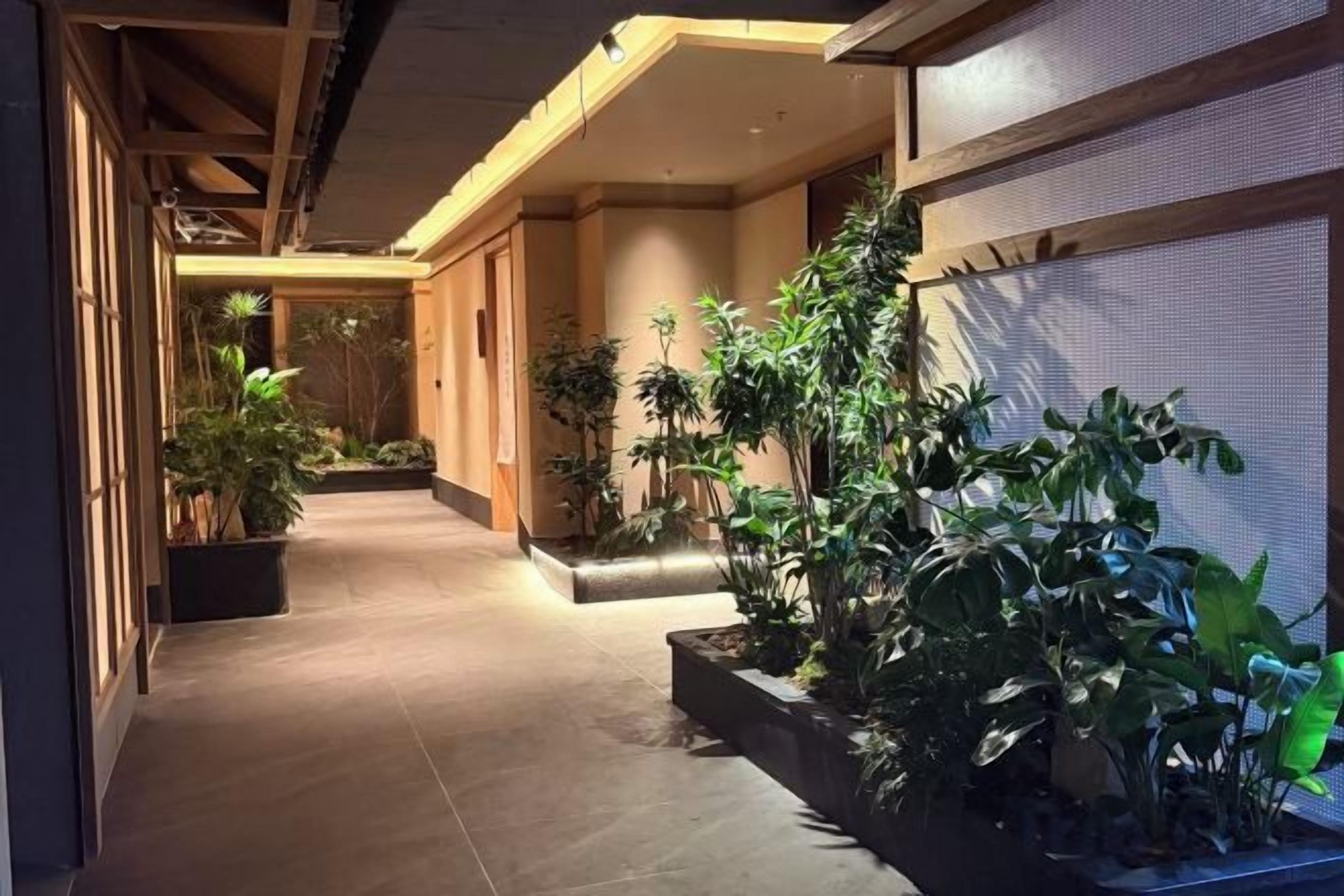 A corridor with potted plants, wooden flooring, and a ceiling with exposed beams.