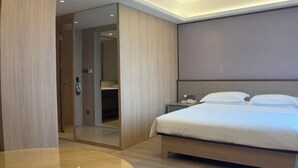 A modern hotel room with a bed, a bedside table, a mirror, and a door leading to a bathroom. - Yilin International Hotel (Hefei)