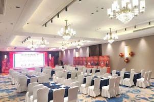 A conference room with rows of tables, white chairs, and chandeliers.