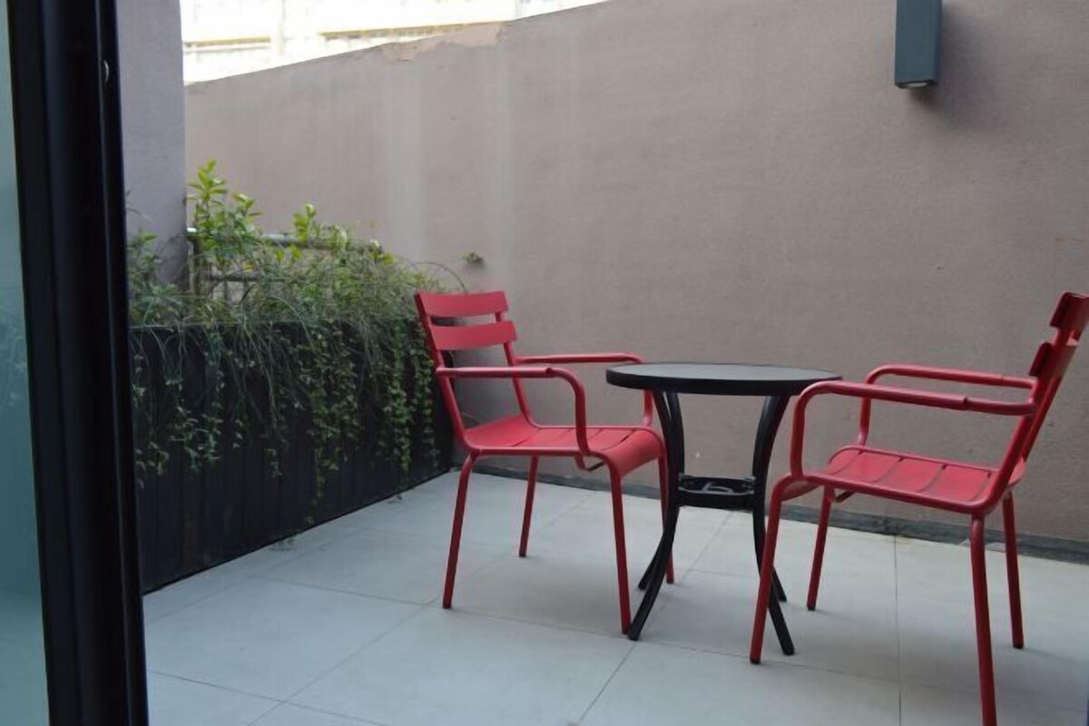 A small patio with two red chairs and a table, surrounded by a low wall and some greenery.