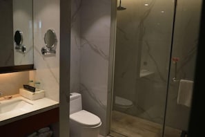 A bathroom with a marble wall, a toilet, a sink, and a glass-enclosed shower area. - Yilin International Hotel (Hefei)