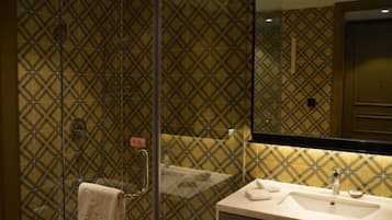 A bathroom with a patterned tile wall, a glass shower enclosure, and a sink with a mirror above it.
