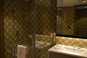 A bathroom with a patterned tile wall, a glass shower enclosure, and a sink with a mirror above it. - Yilin International Hotel (Hefei)