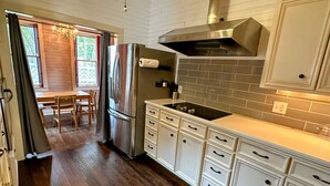 A modern kitchen with white cabinetry, a stainless steel refrigerator, and a black stovetop. - Casa Tejas in Taylor TX (Taylor)