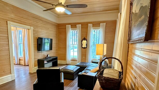 A spacious living room with a wooden floor, a ceiling fan, a flat-screen TV, a sofa, a coffee table, and a large painting on the wall. - Casa Tejas in Taylor TX (Taylor)