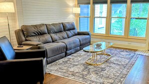 A living room with a leather sofa, a glass coffee table, a patterned rug, and a view of the outdoors through large windows. - Casa Tejas in Taylor TX (Taylor)