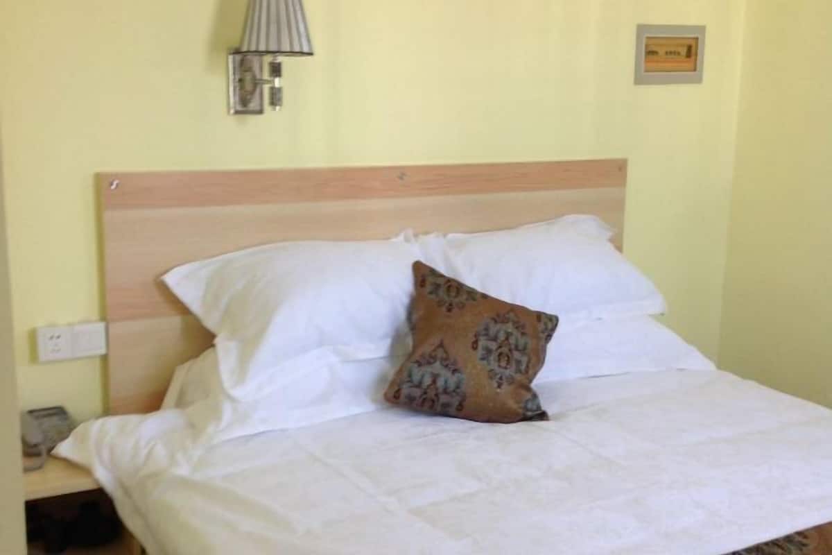 A bed with white bedding and a patterned pillow, a nightstand with a lamp, and a wall-mounted light fixture.