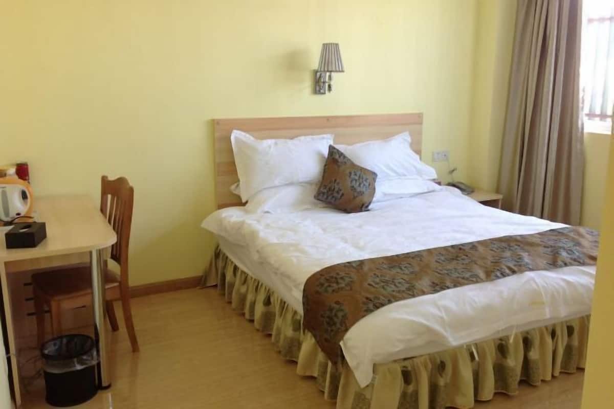 A hotel room with a bed, a desk, a chair, a lamp, and a trash bin.