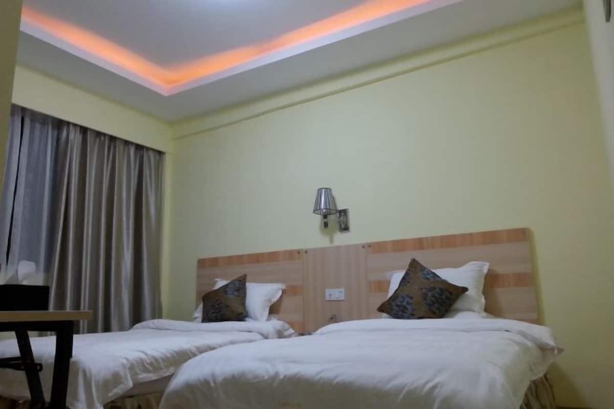 A hotel room with two beds, a bedside table, a lamp, and a window with curtains.
