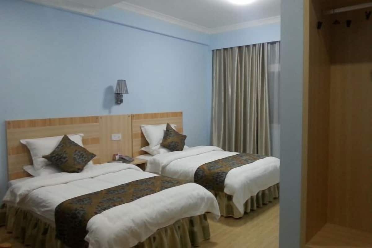A hotel room with two beds, a wooden headboard, a nightstand, a lamp, and a window with curtains.