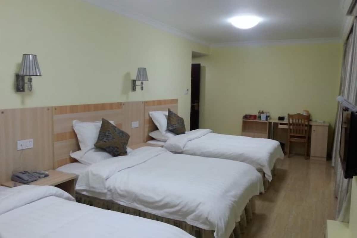 A hotel room with three single beds, a desk, and two wall-mounted lamps.