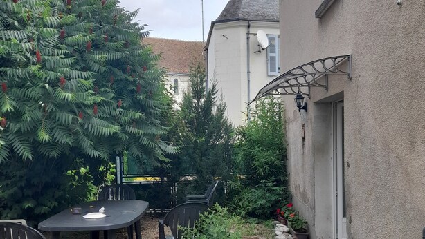 Un patio con tavolo e sedie, circondato da piante in vaso e un piccolo giardino.