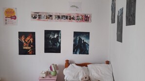 Una camera da letto con un letto in legno, un comodino rosa e dei poster appesi alle pareti.
