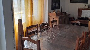 Zona pranzo con tavolo rotondo, sedie in legno, un pianoforte e un quadro appeso al muro.