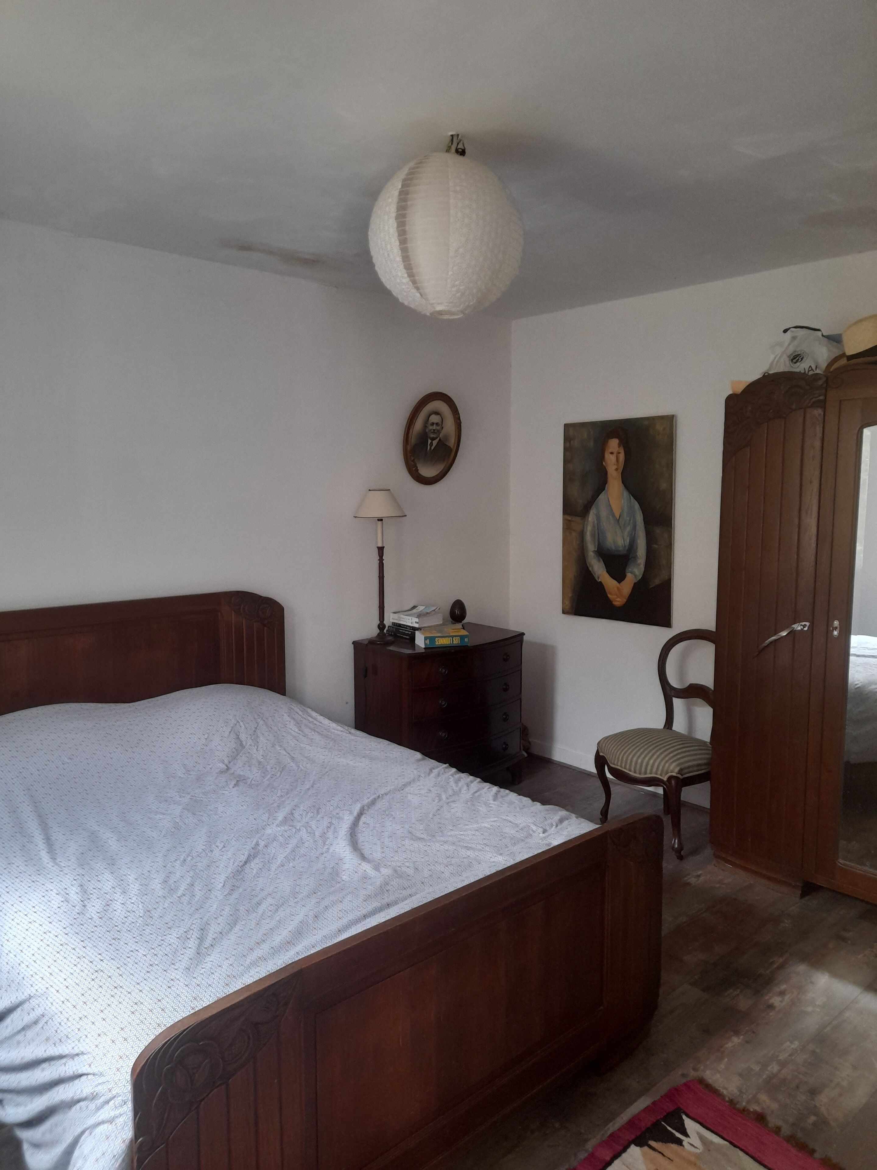 Une chambre à coucher avec un lit en bois, une commode, une chaise, une lampe et un tableau accroché au mur.