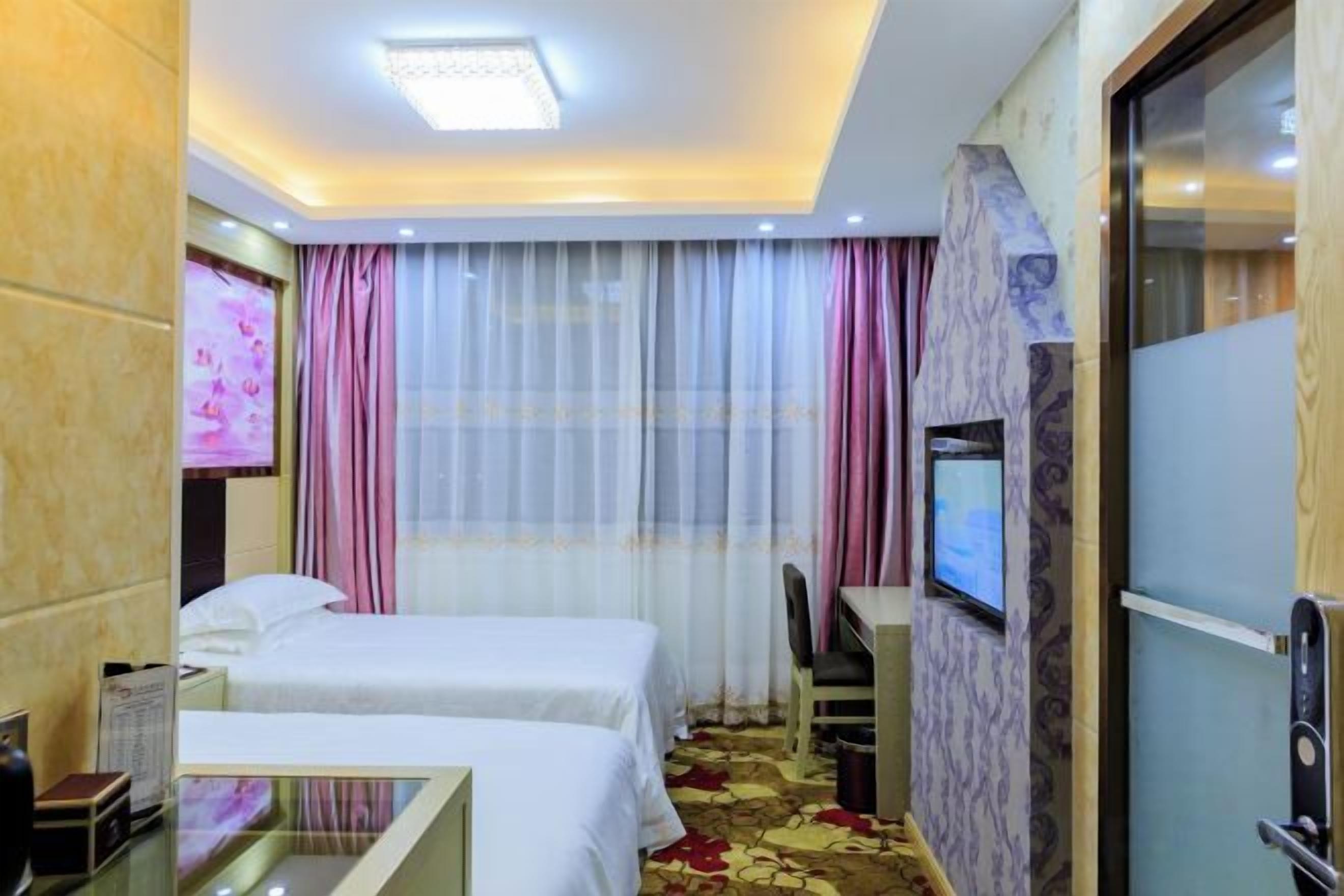 Une chambre d’hôtel avec deux lits, une télévision, un bureau et une porte vitrée donnant sur une salle de bain.