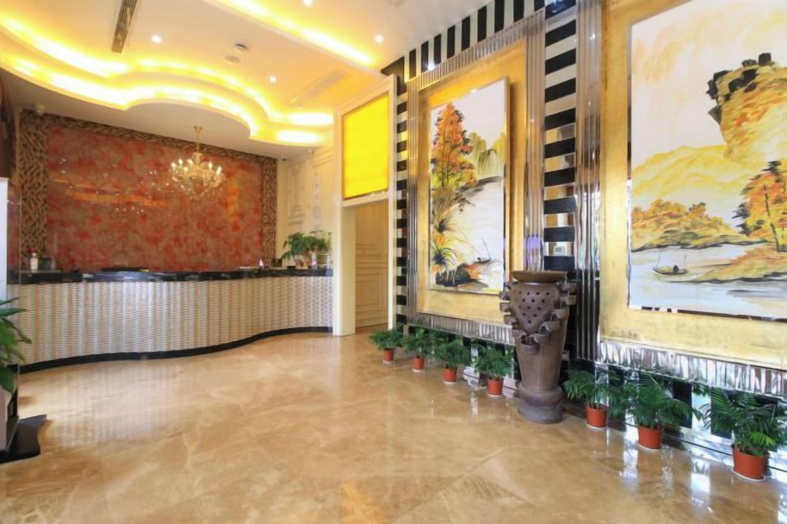 Un hall d’hôtel avec un comptoir d’accueil, un grand tableau et des plantes en pot.