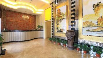 Un hall d’hôtel avec un comptoir d’accueil, un grand tableau et des plantes en pot.