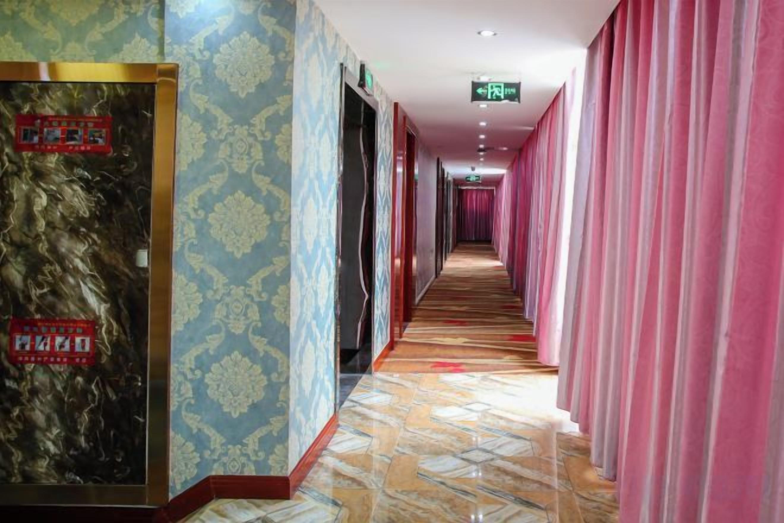 Un pasillo de hotel con paredes estampadas, piso de baldosas y cortinas rosadas.