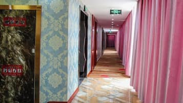 Ein Hotelgang mit gemusterten Wänden, Fliesenboden und rosafarbenen Vorhängen.