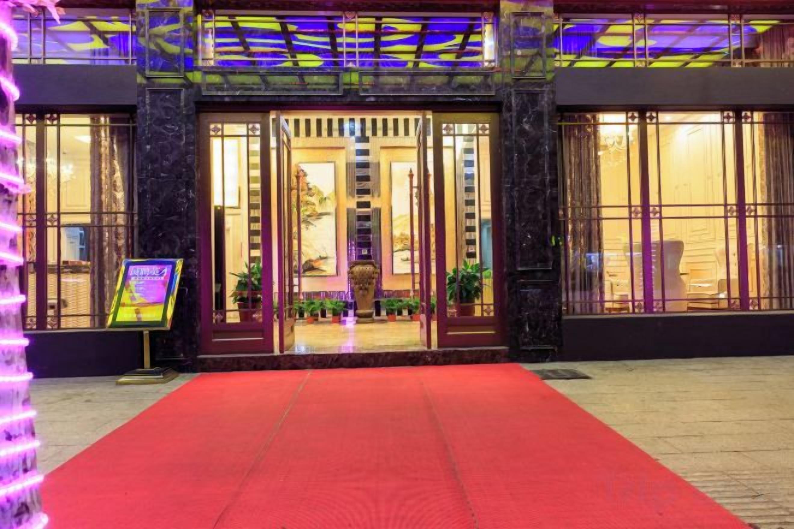 L’entrée d’un hôtel, avec un tapis rouge, de grandes portes vitrées et un panneau indicateur.