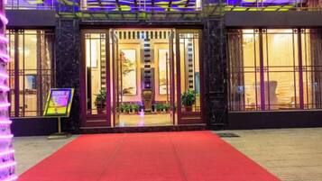 L’entrée d’un hôtel, avec un tapis rouge, de grandes portes vitrées et un panneau indicateur.