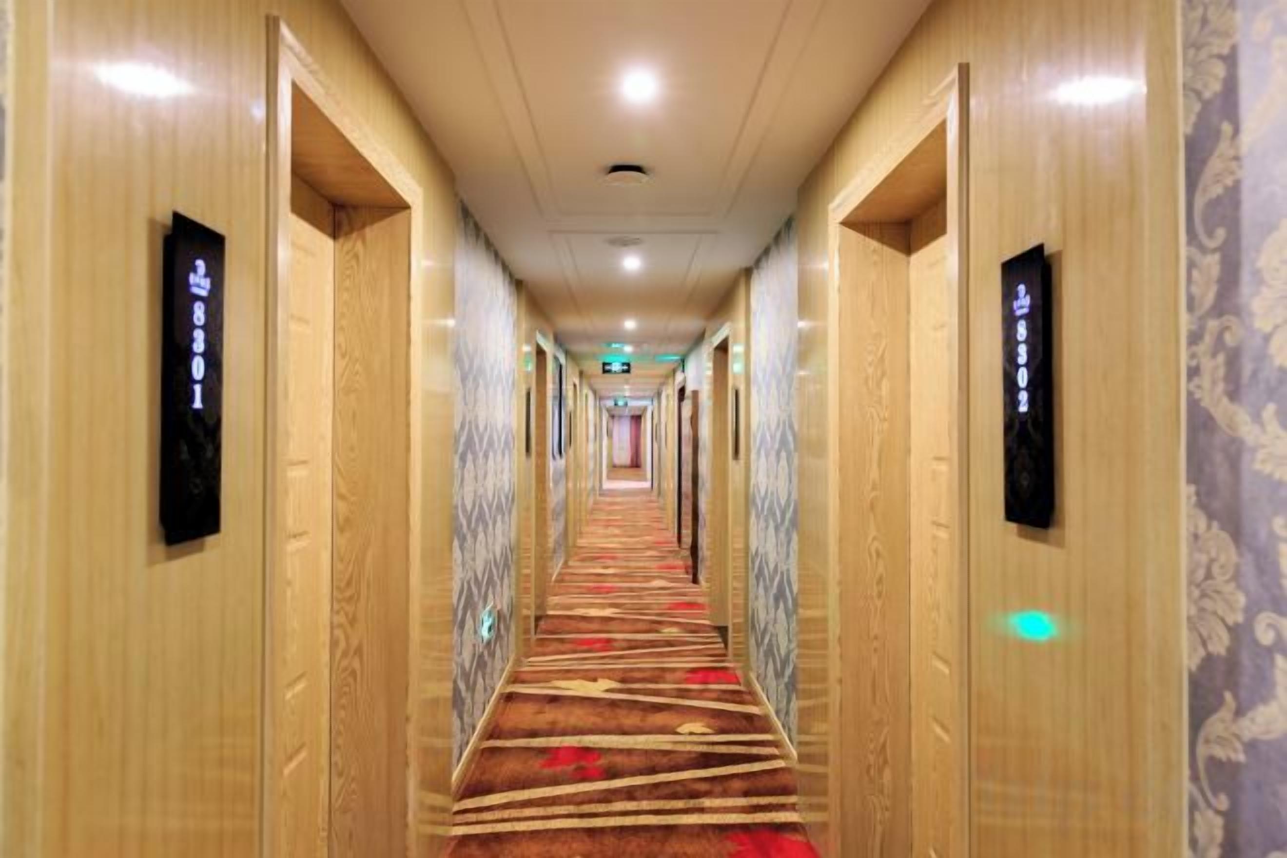 A hotel hallway with carpeted floors, wooden walls, and doors with room numbers.