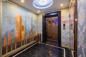 A hotel lobby with a mural, an elevator, and a trash bin. - Aifeng Hotel (Yiwu Gongren North Road) (Yiwu)