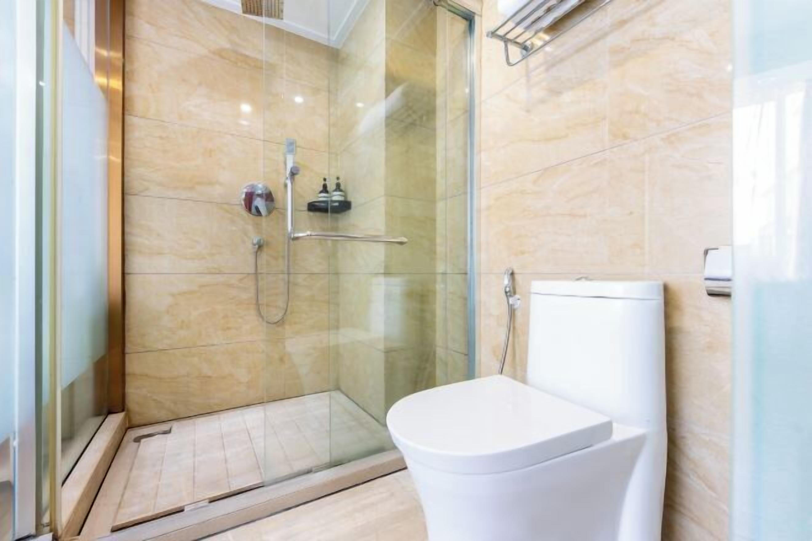 A modern bathroom with a glass shower enclosure, a white toilet, and a marble-tiled wall.