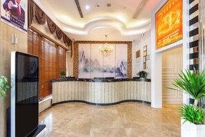 A hotel reception area with a curved reception desk, a flat-screen TV, a chandelier, and a large framed artwork on the wall. - Aifeng Hotel (Yiwu Gongren North Road) (Yiwu)