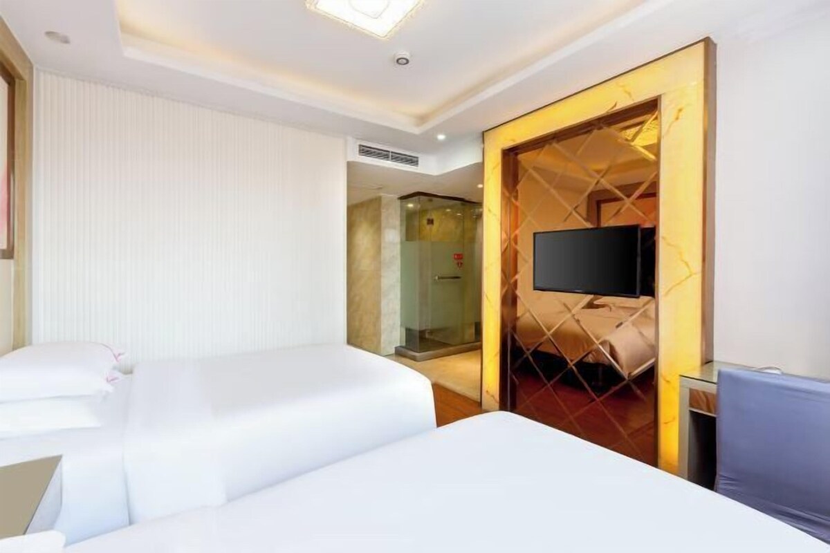 A hotel room with two beds, a TV, and a glass shower enclosure.