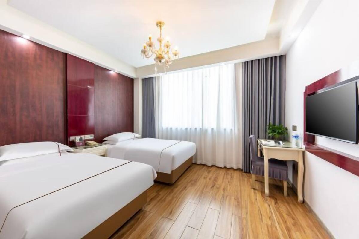 Une chambre d’hôtel avec deux lits, un bureau, une télévision et un lustre.