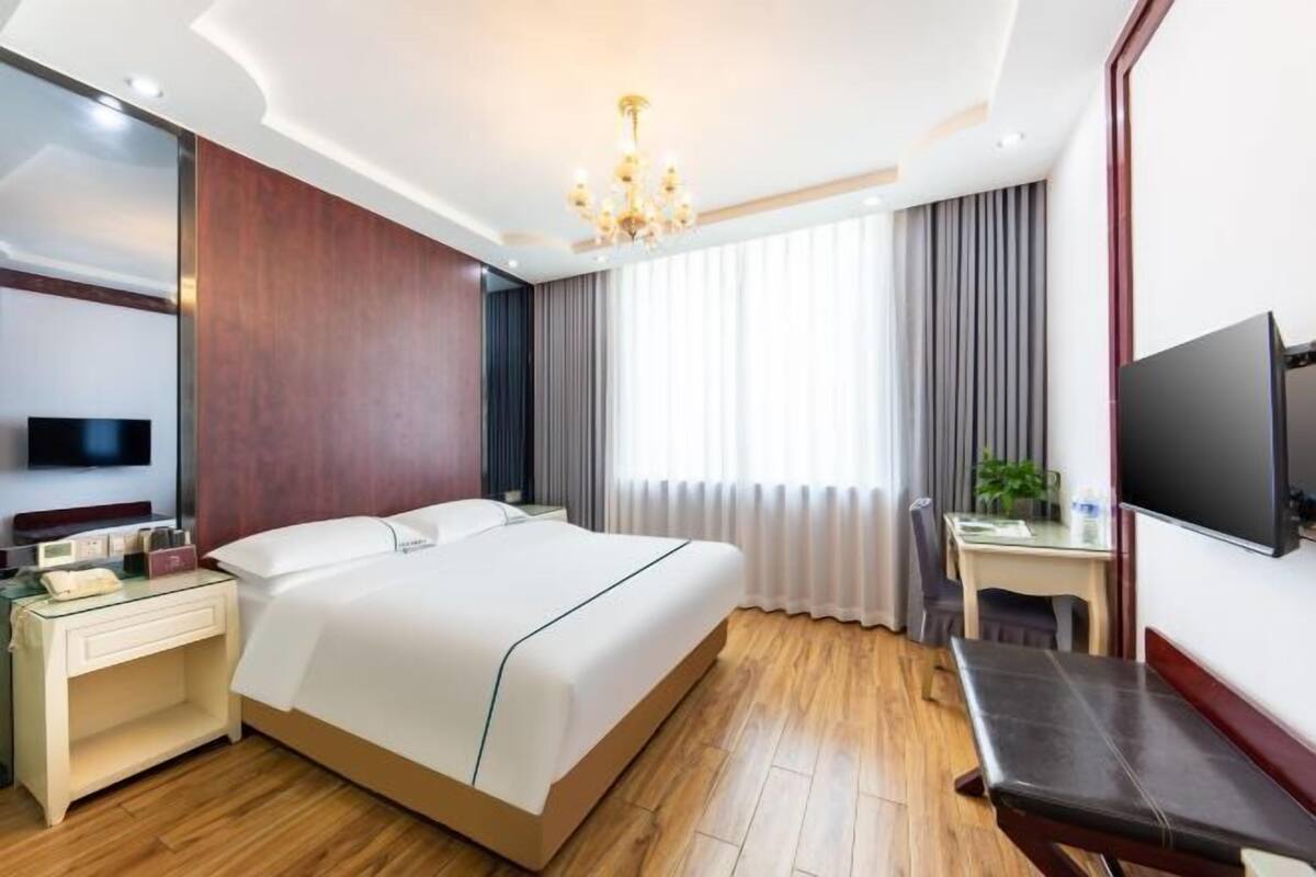 Une chambre d’hôtel avec un grand lit, un bureau, une télévision et un lustre.