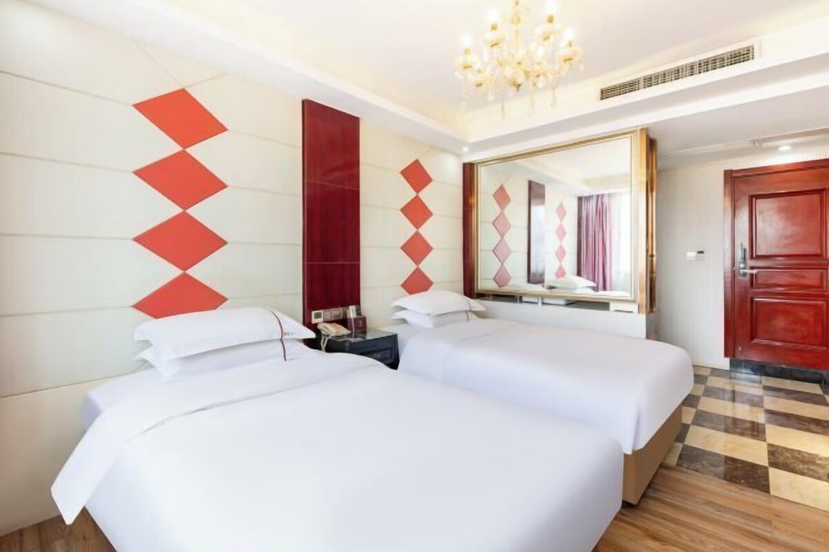 A hotel room with two beds, a large mirror, and a chandelier.