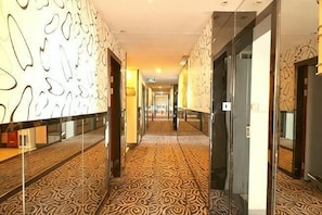 A hotel corridor with patterned carpet, glass doors, and a mirrored wall. - Aifeng Hotel (Yiwu Gongren North Road) (Yiwu)