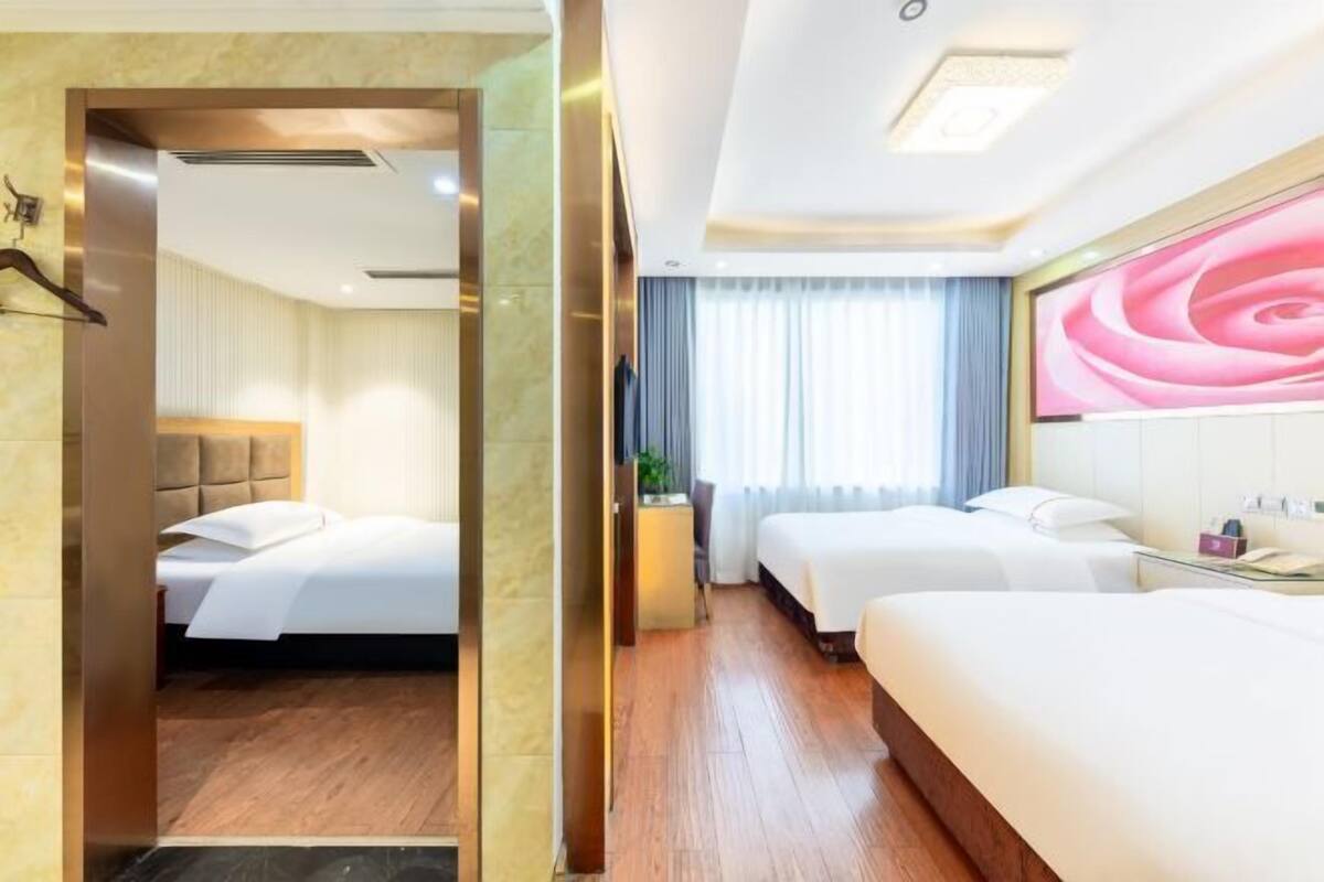 Une chambre d’hôtel avec deux lits, un grand miroir, un bureau avec une lampe et une vue sur l’extérieur par la fenêtre.