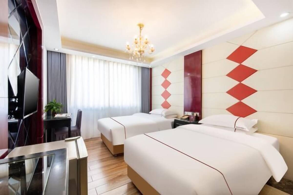 Une chambre d’hôtel avec deux lits, un bureau, une télévision et un lustre.