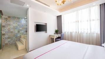 A hotel room with a large bed, a desk, a chair, a TV, and a shower area.