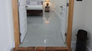 A hallway leading to a bedroom with a bed, a nightstand, and a lamp. There is a trash can and a door with a small picture on it. - Hidden Gem in Historic Downtown Moultrie!  (Moultrie)