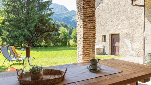 Ein Holztisch im Freien mit Blick auf eine gebirgige Landschaft, eine Steinmauer und eine Tür.