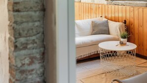 Ein gemütliches Zimmer mit einer Holzwand, einem weißen Sofa und einem runden Tisch mit Metallgestell und einer Pflanze.
